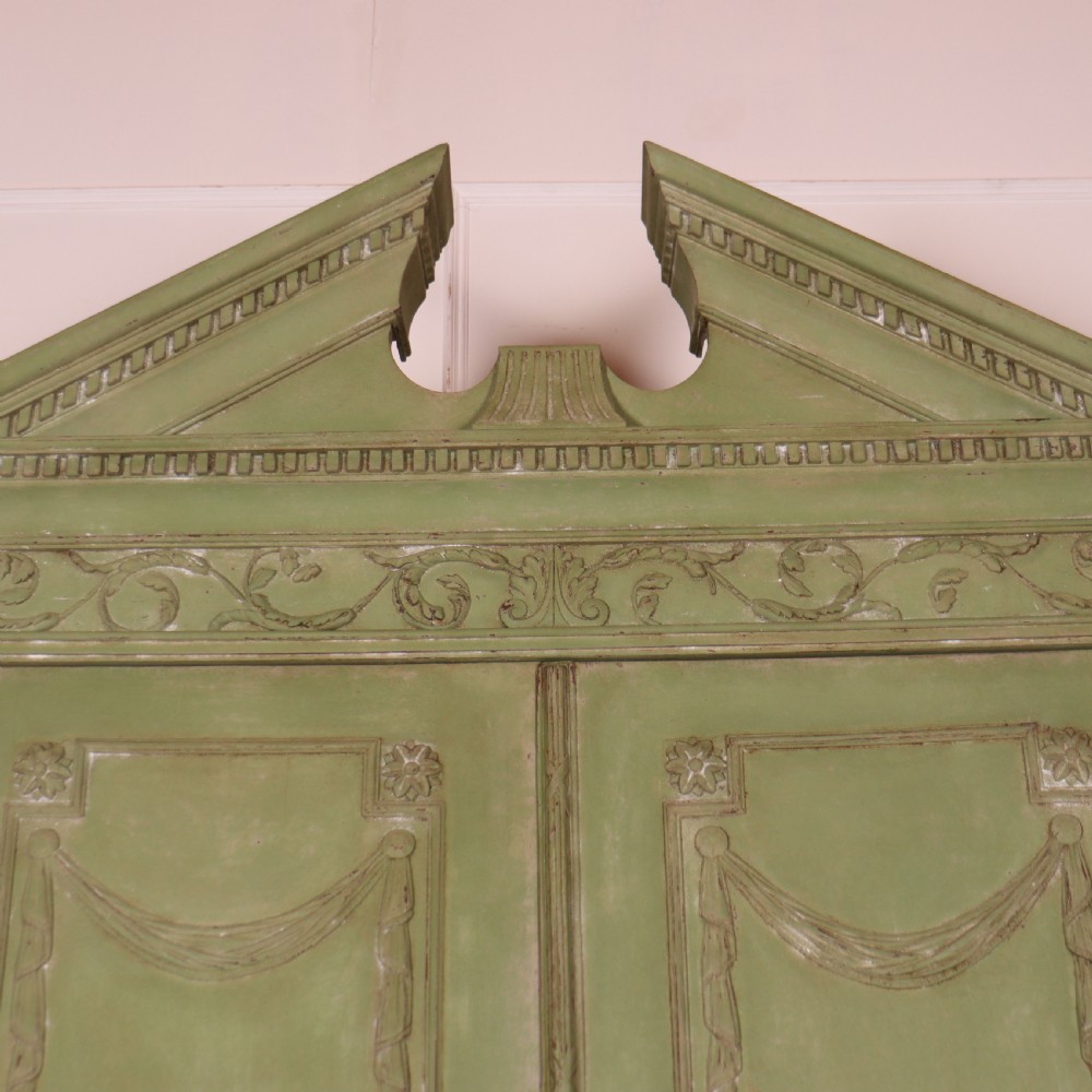 A large sage green painted Dutch linen cupboard featuring a broken pediment cornice, carved swag door panels, brass drop handles, and three lower drawers. View V
