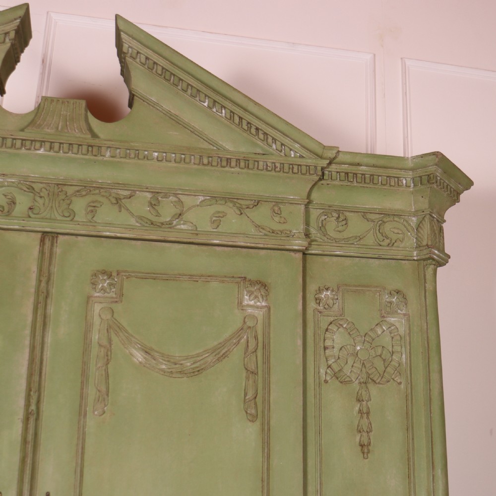 A large sage green painted Dutch linen cupboard featuring a broken pediment cornice, carved swag door panels, brass drop handles, and three lower drawers. View VI
