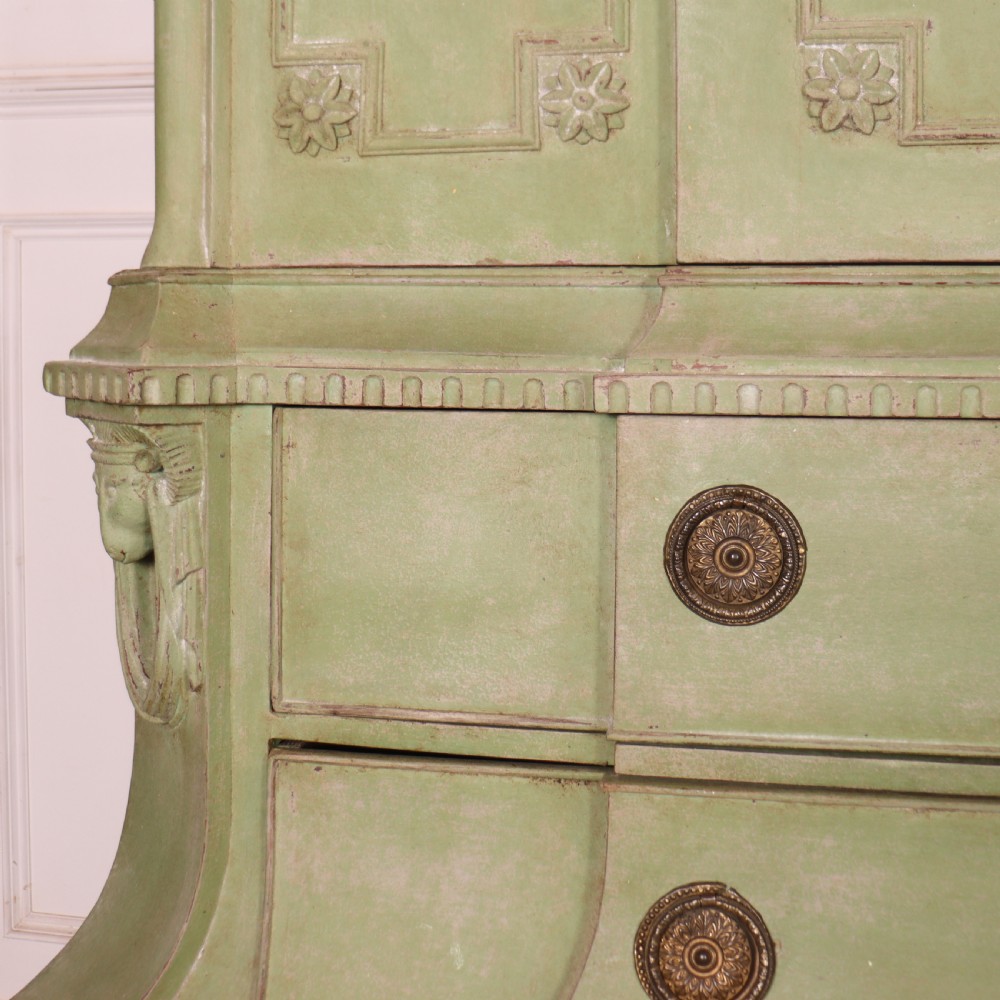 A large sage green painted Dutch linen cupboard featuring a broken pediment cornice, carved swag door panels, brass drop handles, and three lower drawers. View VII