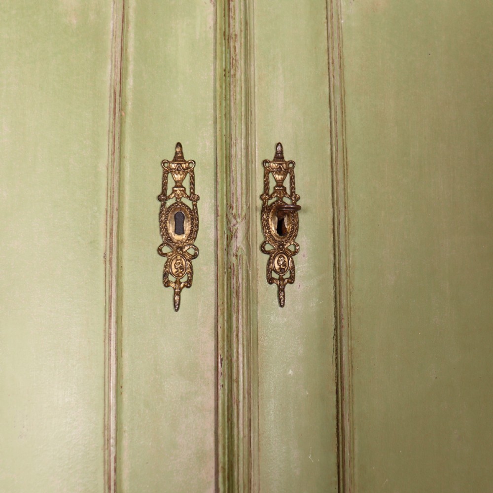 A large sage green painted Dutch linen cupboard featuring a broken pediment cornice, carved swag door panels, brass drop handles, and three lower drawers. View IX