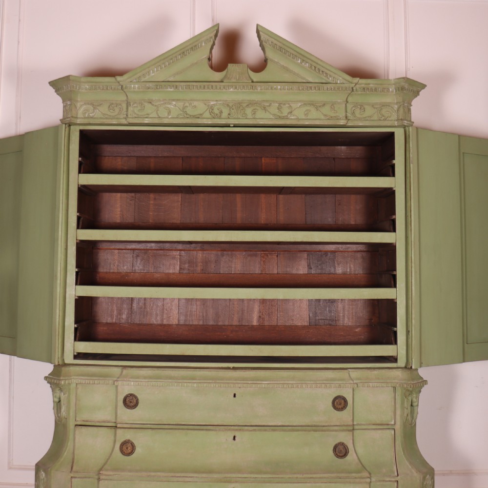 A large sage green painted Dutch linen cupboard featuring a broken pediment cornice, carved swag door panels, brass drop handles, and three lower drawers. View X