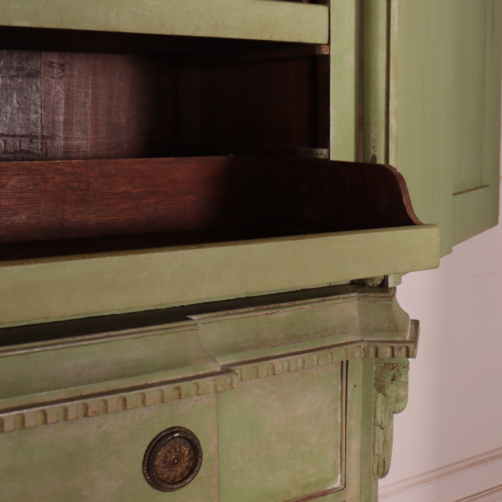 A large sage green painted Dutch linen cupboard featuring a broken pediment cornice, carved swag door panels, brass drop handles, and three lower drawers. View XI