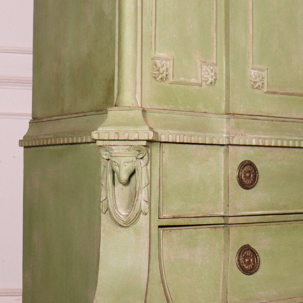 A large sage green painted Dutch linen cupboard featuring a broken pediment cornice, carved swag door panels, brass drop handles, and three lower drawers. View XIII