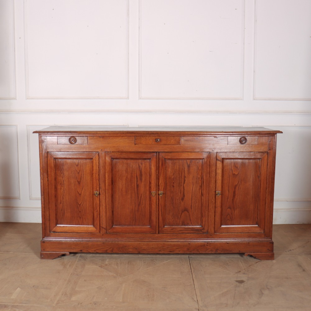 A long French oak enfilade sideboard featuring four field-panel cupboard doors, upper drawers, and central brass key escutcheons.
