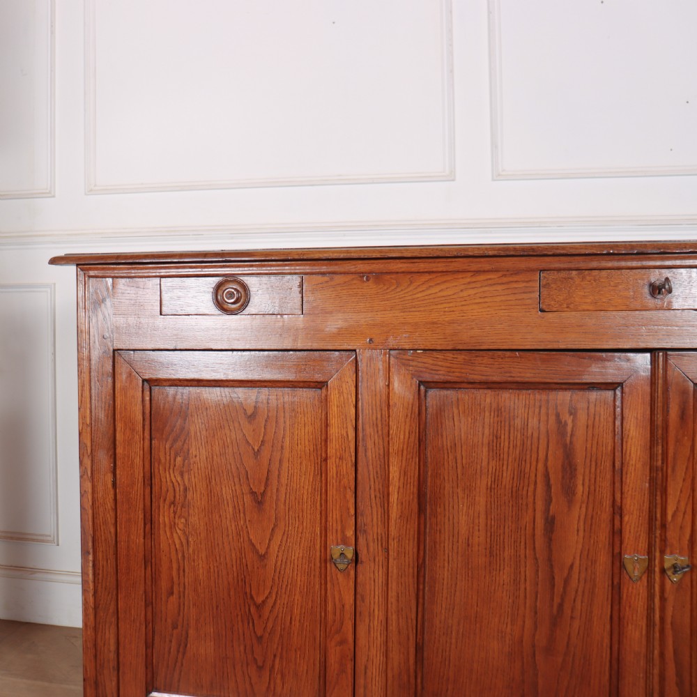 A long French oak enfilade sideboard featuring four field-panel cupboard doors, upper drawers, and central brass key escutcheons. View II