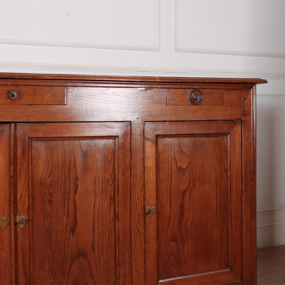 A long French oak enfilade sideboard featuring four field-panel cupboard doors, upper drawers, and central brass key escutcheons. View IV