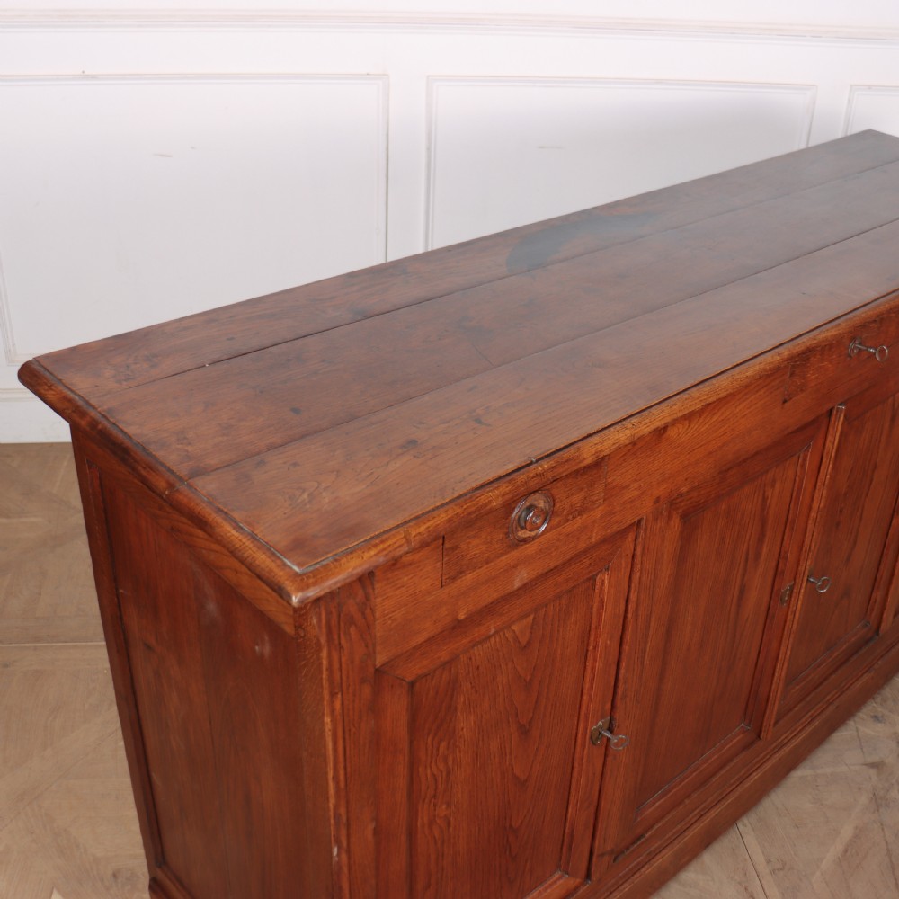 A long French oak enfilade sideboard featuring four field-panel cupboard doors, upper drawers, and central brass key escutcheons. View VIII