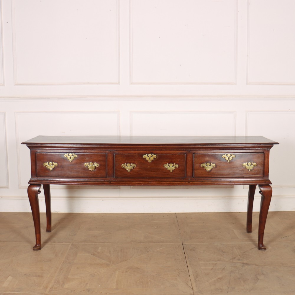 An antique dark oak dresser base featuring three drawers with brass handles and keyhole escutcheons supported on cabriole legs.