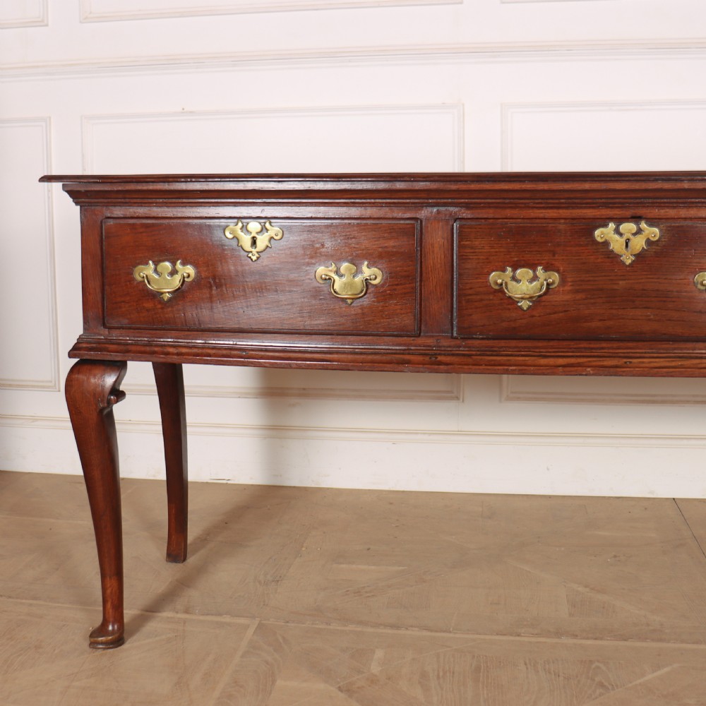 An antique dark oak dresser base featuring three drawers with brass handles and keyhole escutcheons supported on cabriole legs. View II