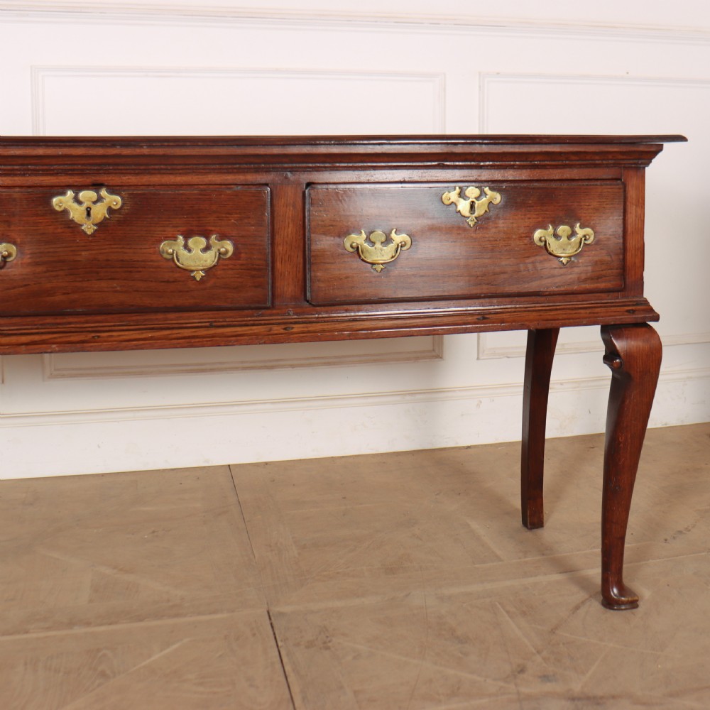 An antique dark oak dresser base featuring three drawers with brass handles and keyhole escutcheons supported on cabriole legs. View V