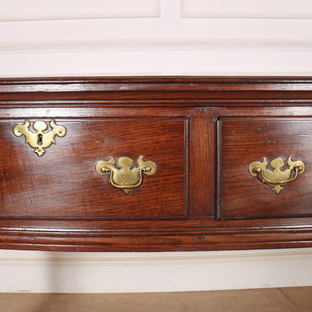 An antique dark oak dresser base featuring three drawers with brass handles and keyhole escutcheons supported on cabriole legs. View VI