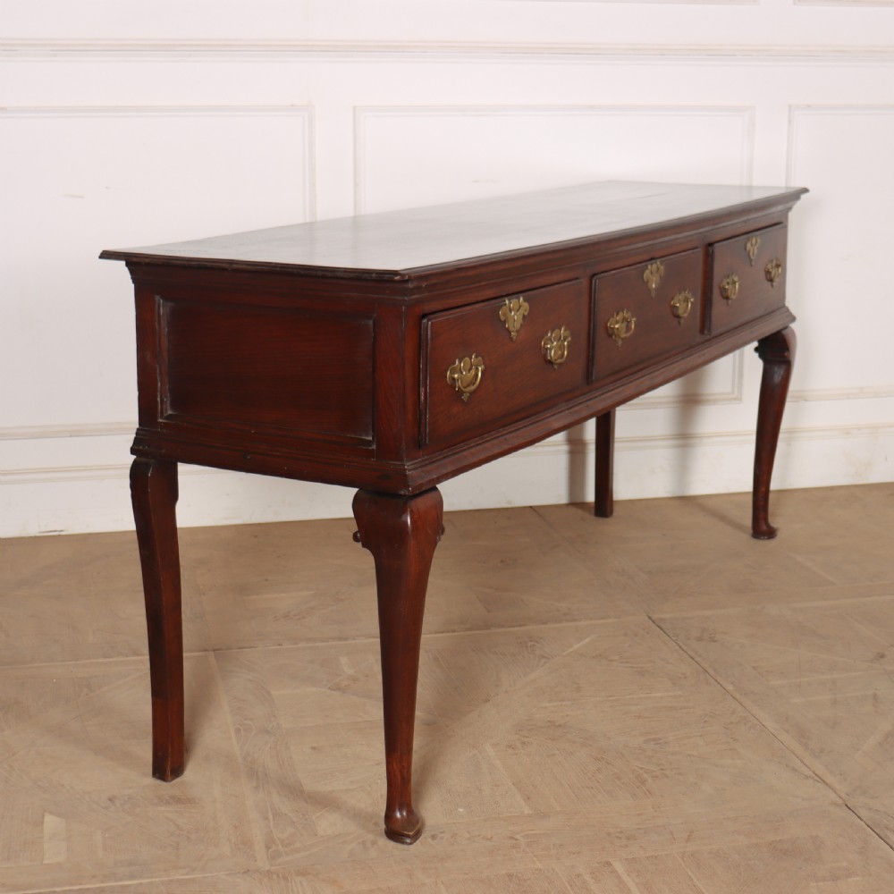 An antique dark oak dresser base featuring three drawers with brass handles and keyhole escutcheons supported on cabriole legs. View VIII