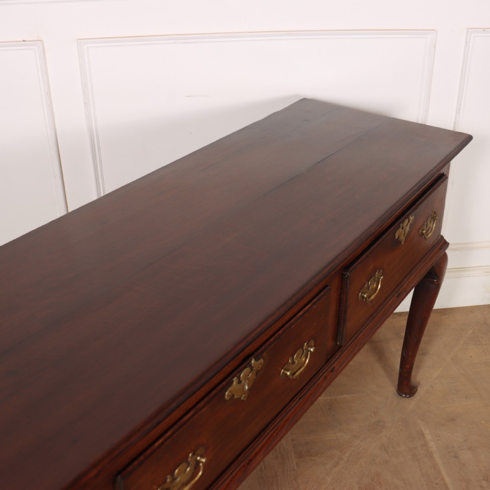 An antique dark oak dresser base featuring three drawers with brass handles and keyhole escutcheons supported on cabriole legs. View X