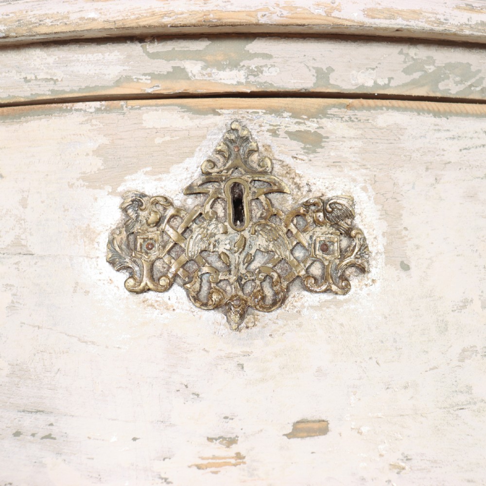 A French painted two-drawer commode featuring a bombe shape, distressed off-white finish, carved apron, cabriole legs, and ornate brass hardware. View II