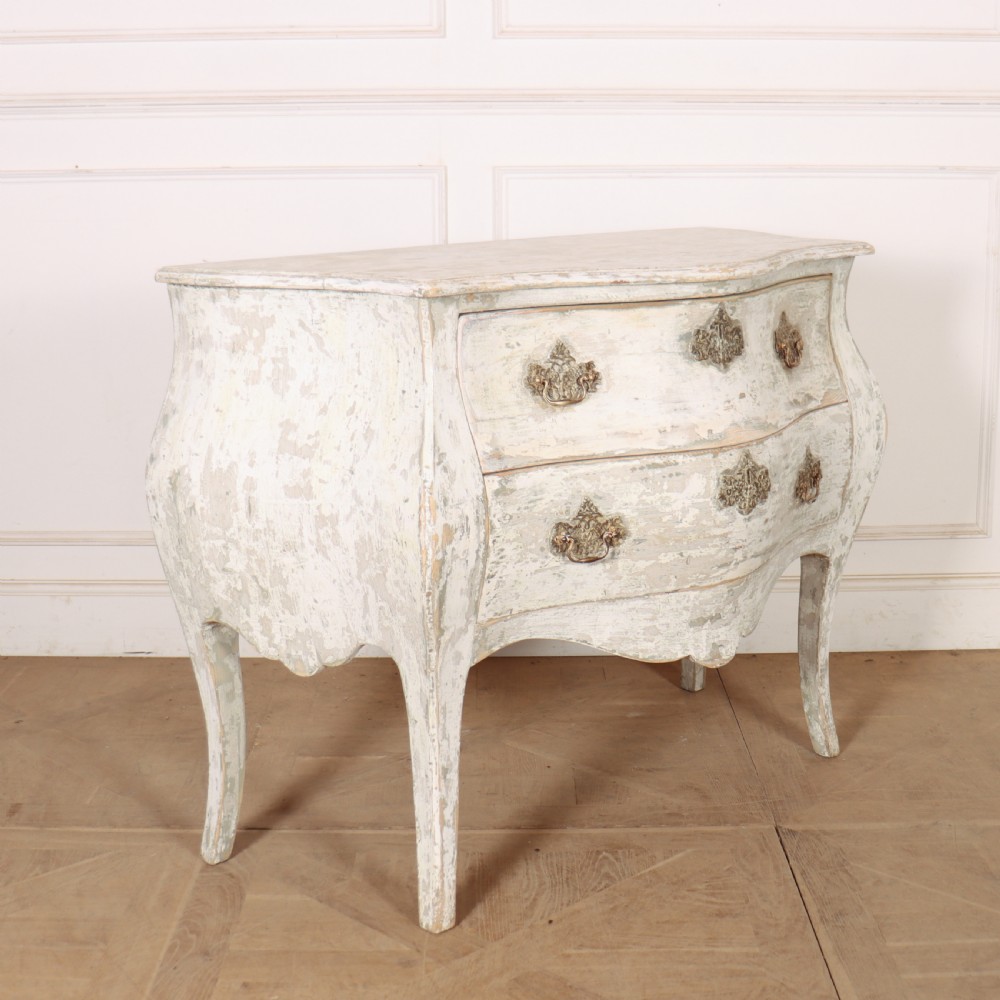 A French painted two-drawer commode featuring a bombe shape, distressed off-white finish, carved apron, cabriole legs, and ornate brass hardware. View III