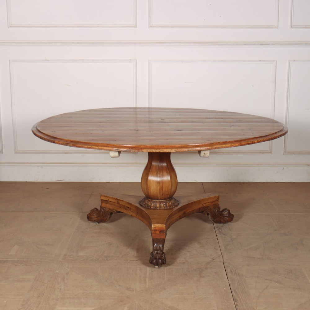 A large 19th-century circular wood supper table featuring a bulbous turned pedestal column and carved paw feet on a triform base.