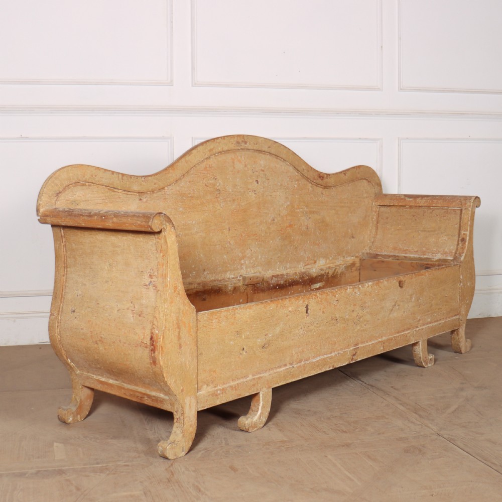 A Swedish wooden storage bench featuring a contoured backrest, rolled armrests, and an open seat box with distressed yellow paint finish.