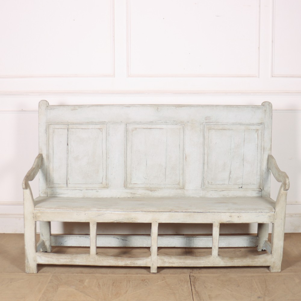 An 18th-century painted wooden tavern bench featuring a high back with three recessed panels, curved armrests, and lower stretchers.