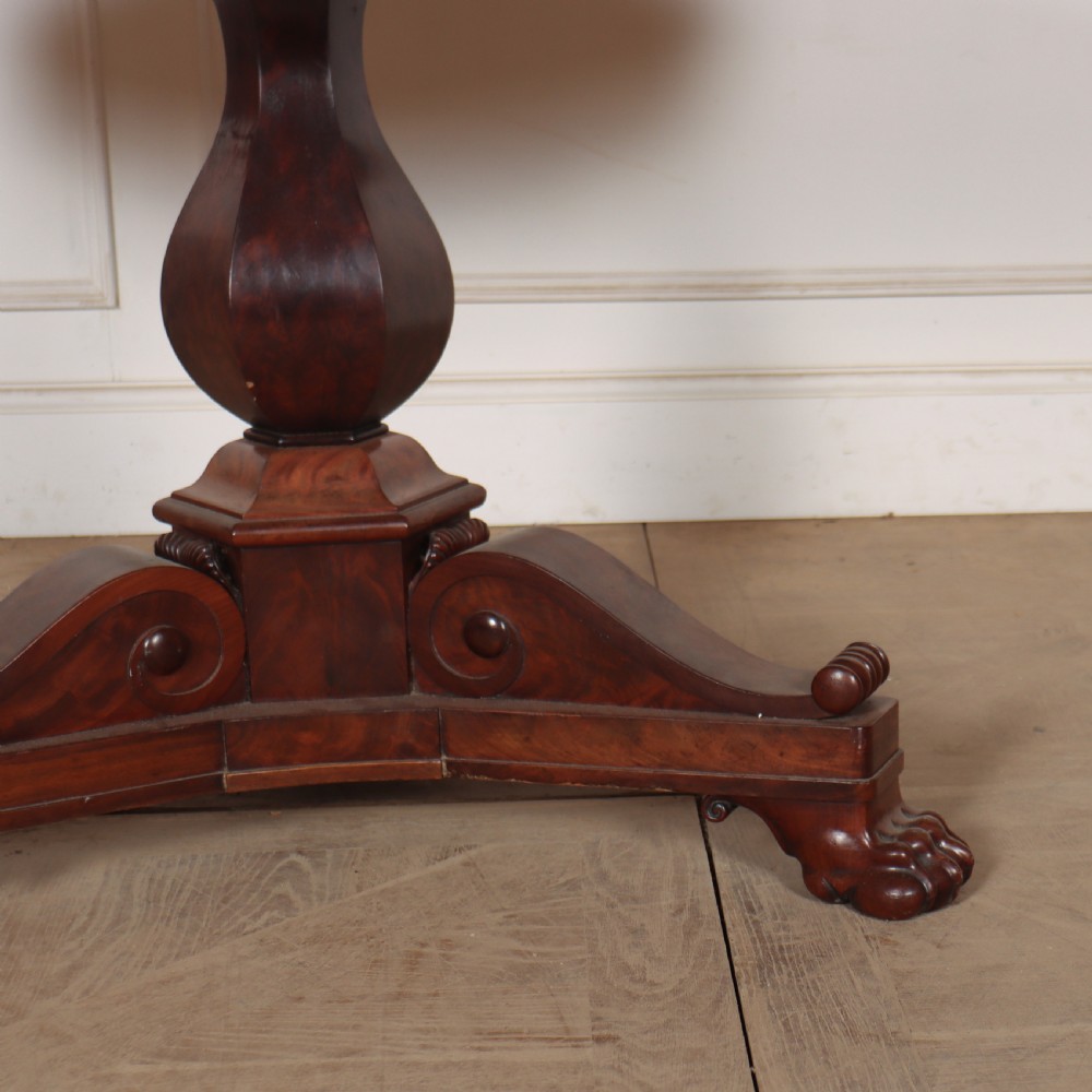 A large circular French gueridon table featuring a dark grey marble top set upon a dark mahogany pedestal base with a triform platform and carved paw feet. View IV