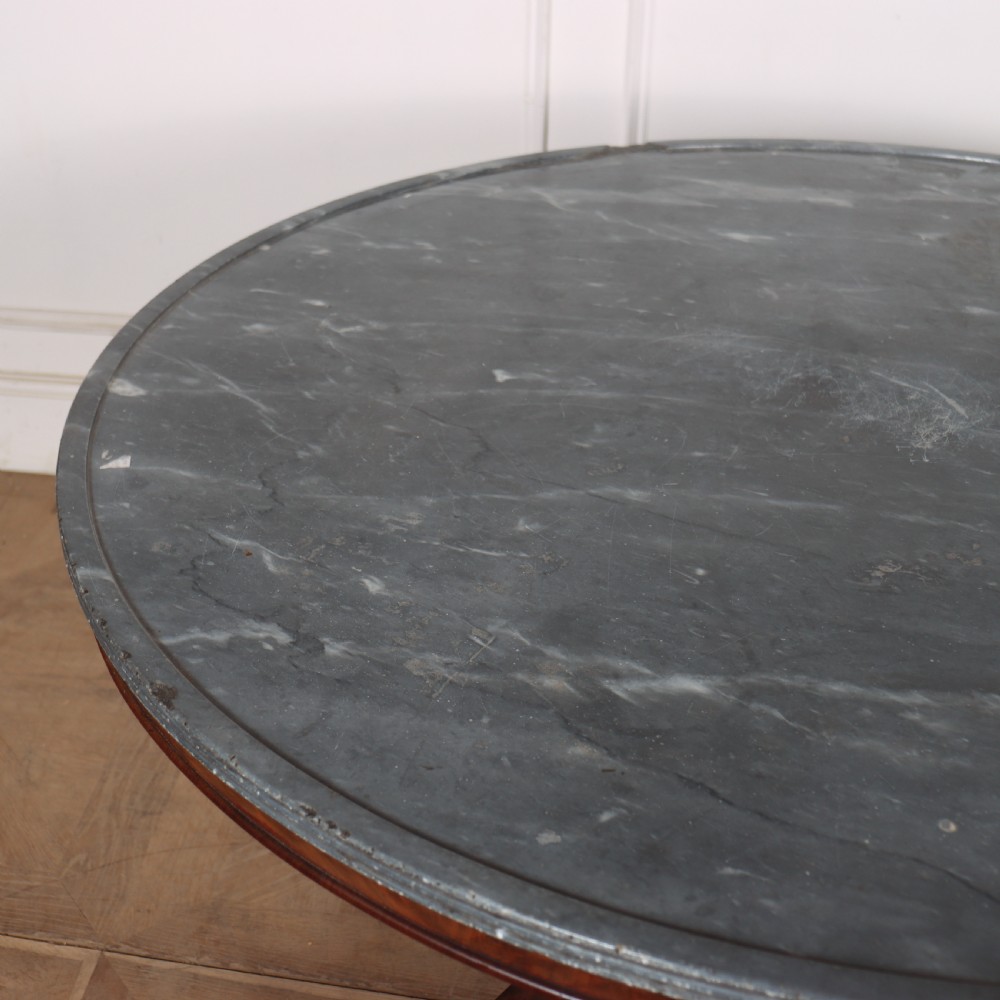 A large circular French gueridon table featuring a dark grey marble top set upon a dark mahogany pedestal base with a triform platform and carved paw feet. View V