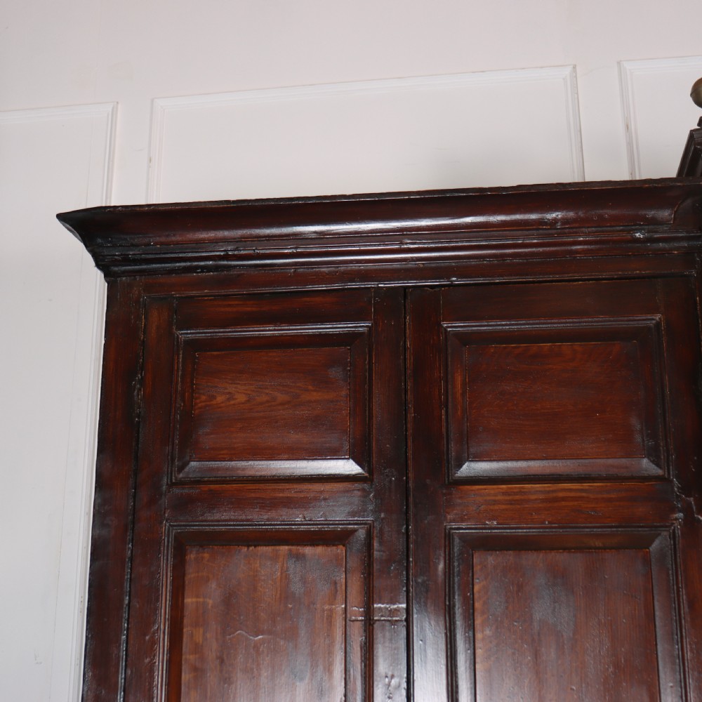 An antique dark brown wooden housekeepers cupboard featuring panelled doors, a central integrated grandfather clock, and a base section with six drawers. View II