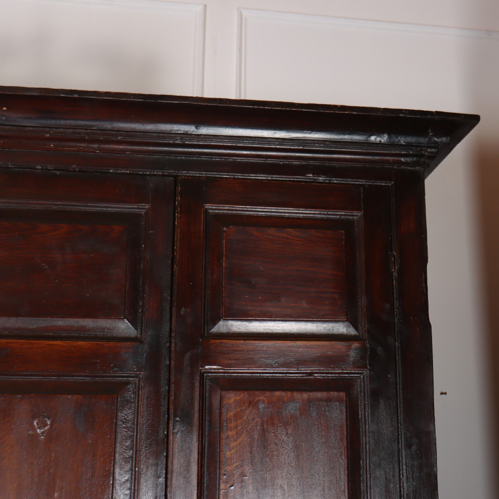 An antique dark brown wooden housekeepers cupboard featuring panelled doors, a central integrated grandfather clock, and a base section with six drawers. View IV