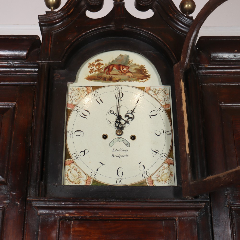 An antique dark brown wooden housekeepers cupboard featuring panelled doors, a central integrated grandfather clock, and a base section with six drawers. View VII
