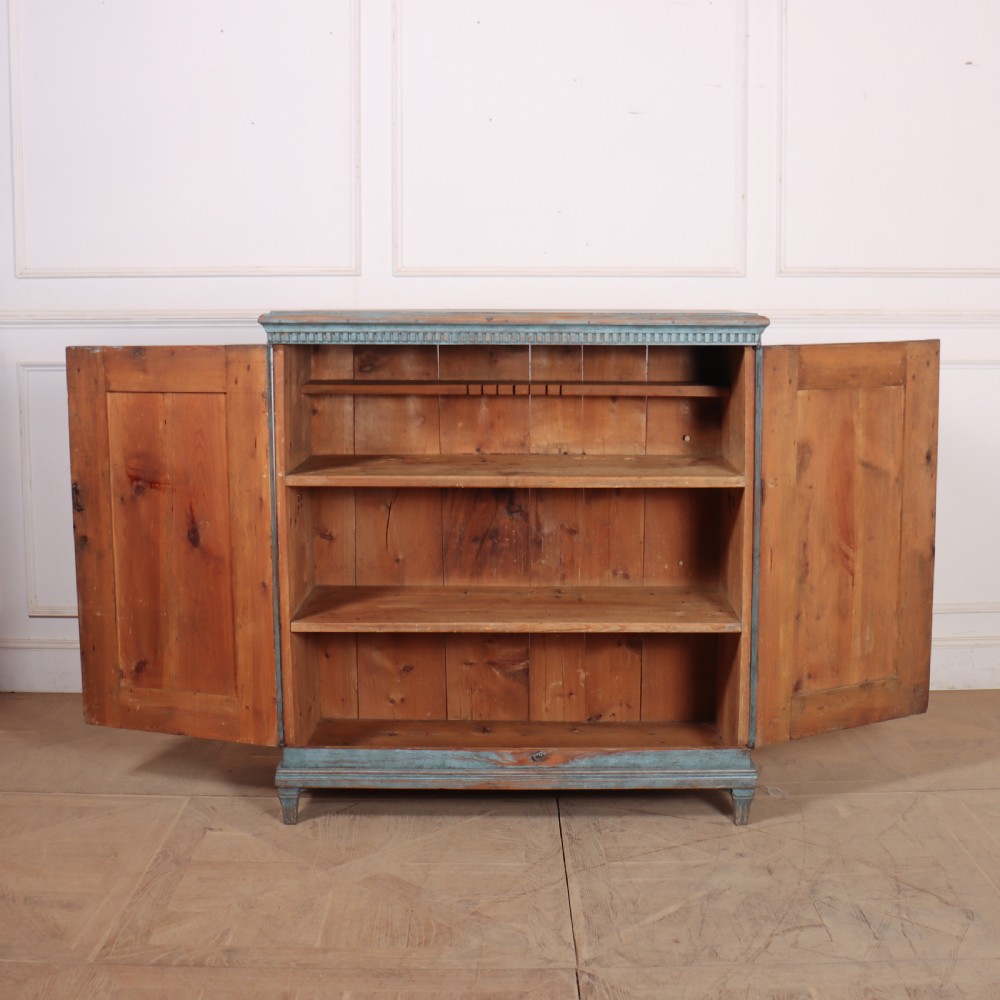 A freestanding Swedish blue painted wooden cupboard featuring two panelled doors, dentil moulding at the cornice, and short tapered feet. View VII