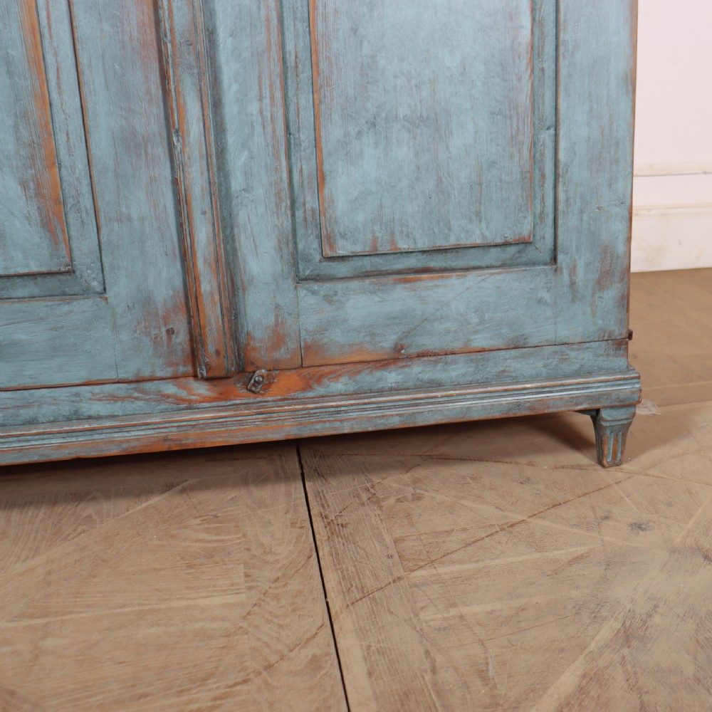 A Swedish two-door wooden cupboard featuring a distressed blue painted finish, panelled doors, dentil moulding along the top frieze, and short tapered legs. View III