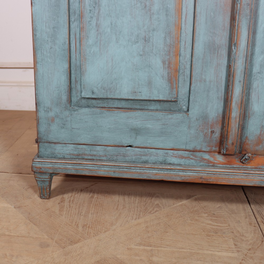 A Swedish two-door wooden cupboard featuring a distressed blue painted finish, panelled doors, dentil moulding along the top frieze, and short tapered legs. View IV