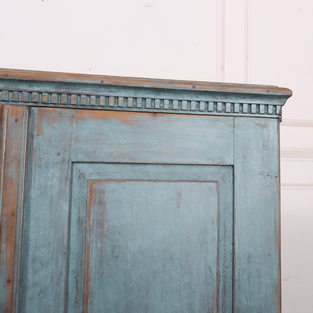 A Swedish two-door wooden cupboard featuring a distressed blue painted finish, panelled doors, dentil moulding along the top frieze, and short tapered legs. View VI
