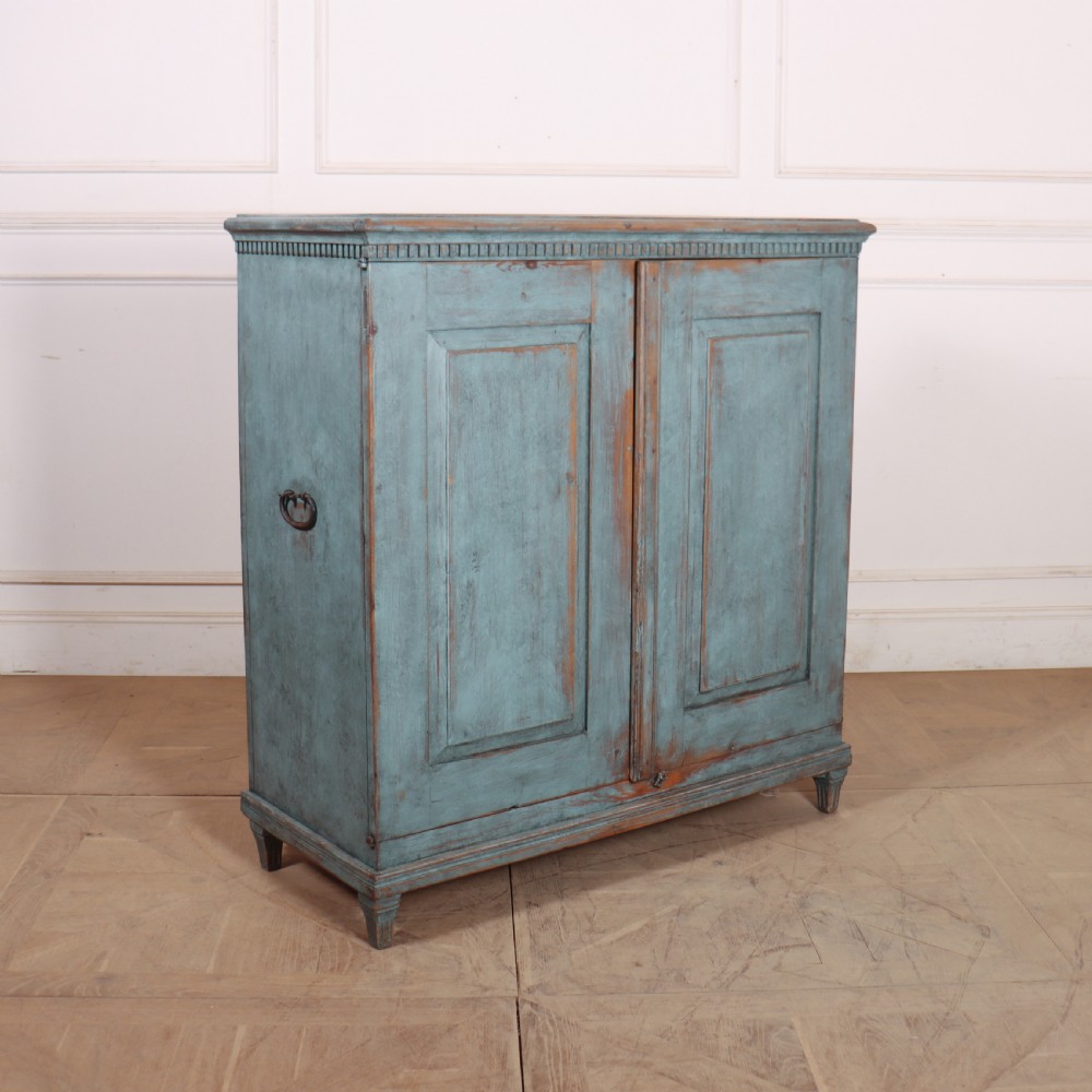 A Swedish two-door wooden cupboard featuring a distressed blue painted finish, panelled doors, dentil moulding along the top frieze, and short tapered legs. View VIII