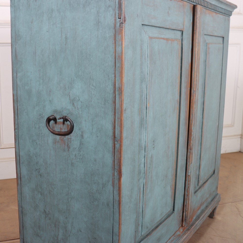 A Swedish two-door wooden cupboard featuring a distressed blue painted finish, panelled doors, dentil moulding along the top frieze, and short tapered legs. View IX