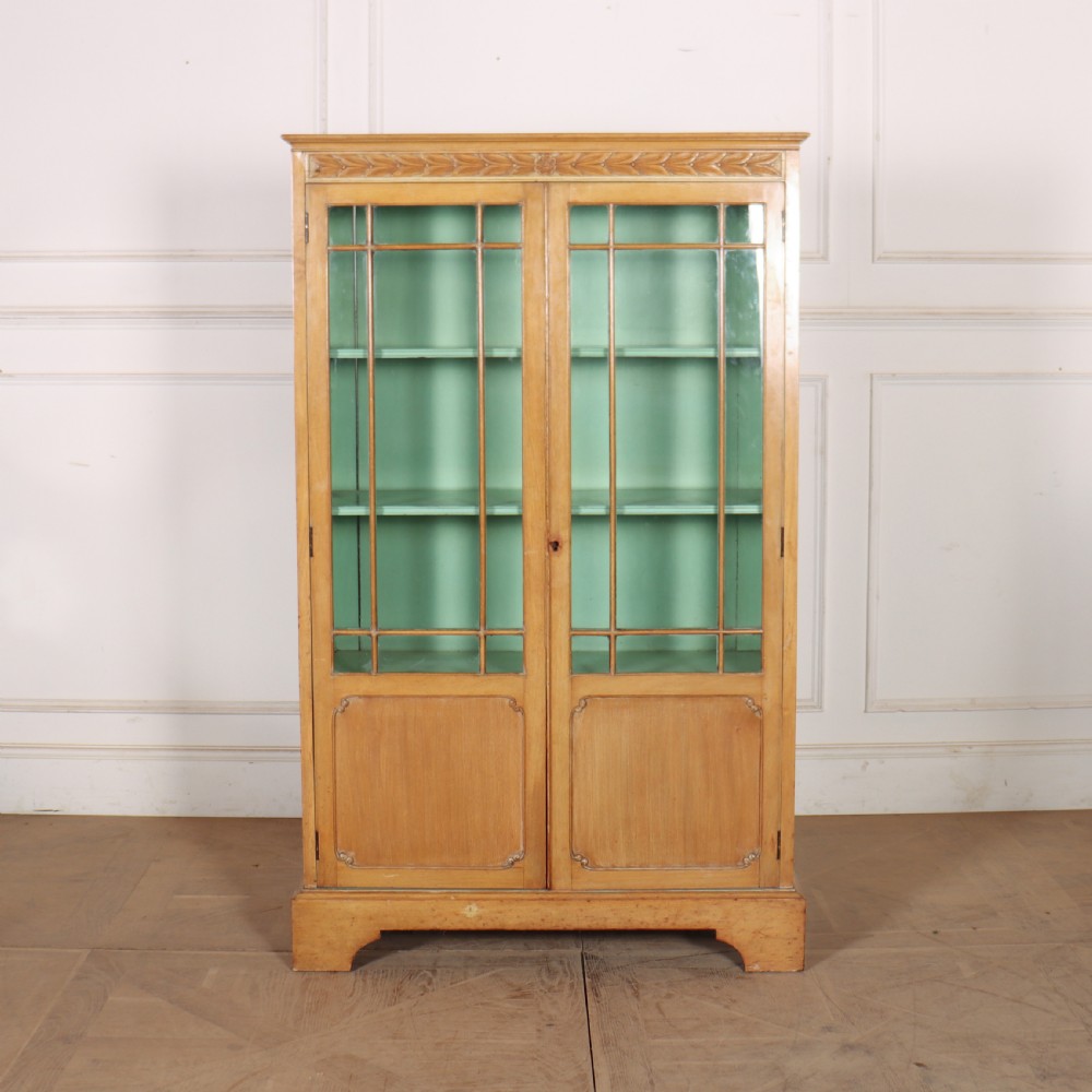 A tall English bleached walnut bookcase featuring two glazed doors with geometric glazing bars, a carved leaf frieze at the top, and a contrasting mint green painted interior. View II