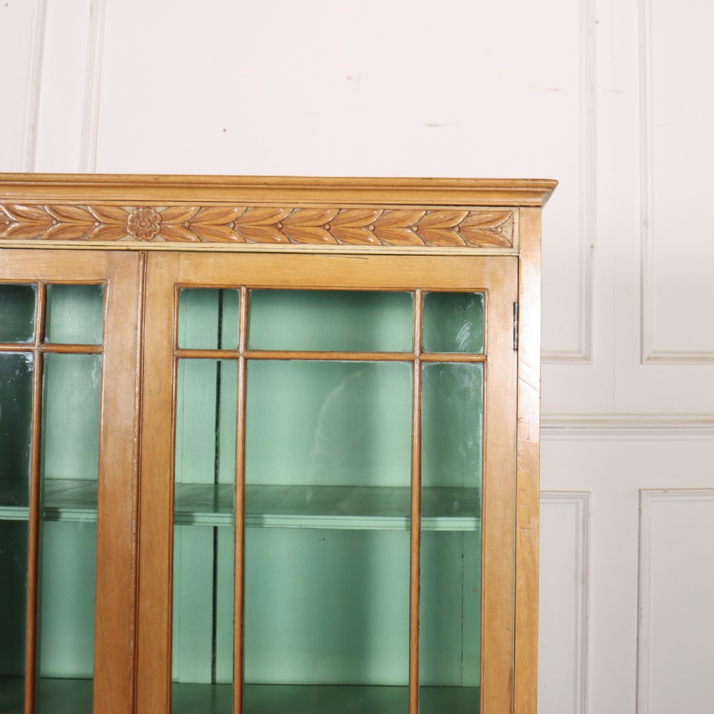 A tall English bleached walnut bookcase featuring two glazed doors with geometric glazing bars, a carved leaf frieze at the top, and a contrasting mint green painted interior. View III