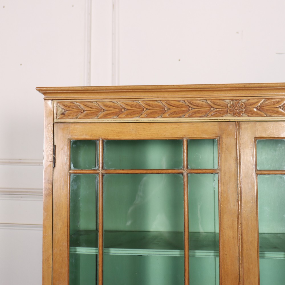 A tall English bleached walnut bookcase featuring two glazed doors with geometric glazing bars, a carved leaf frieze at the top, and a contrasting mint green painted interior. View V