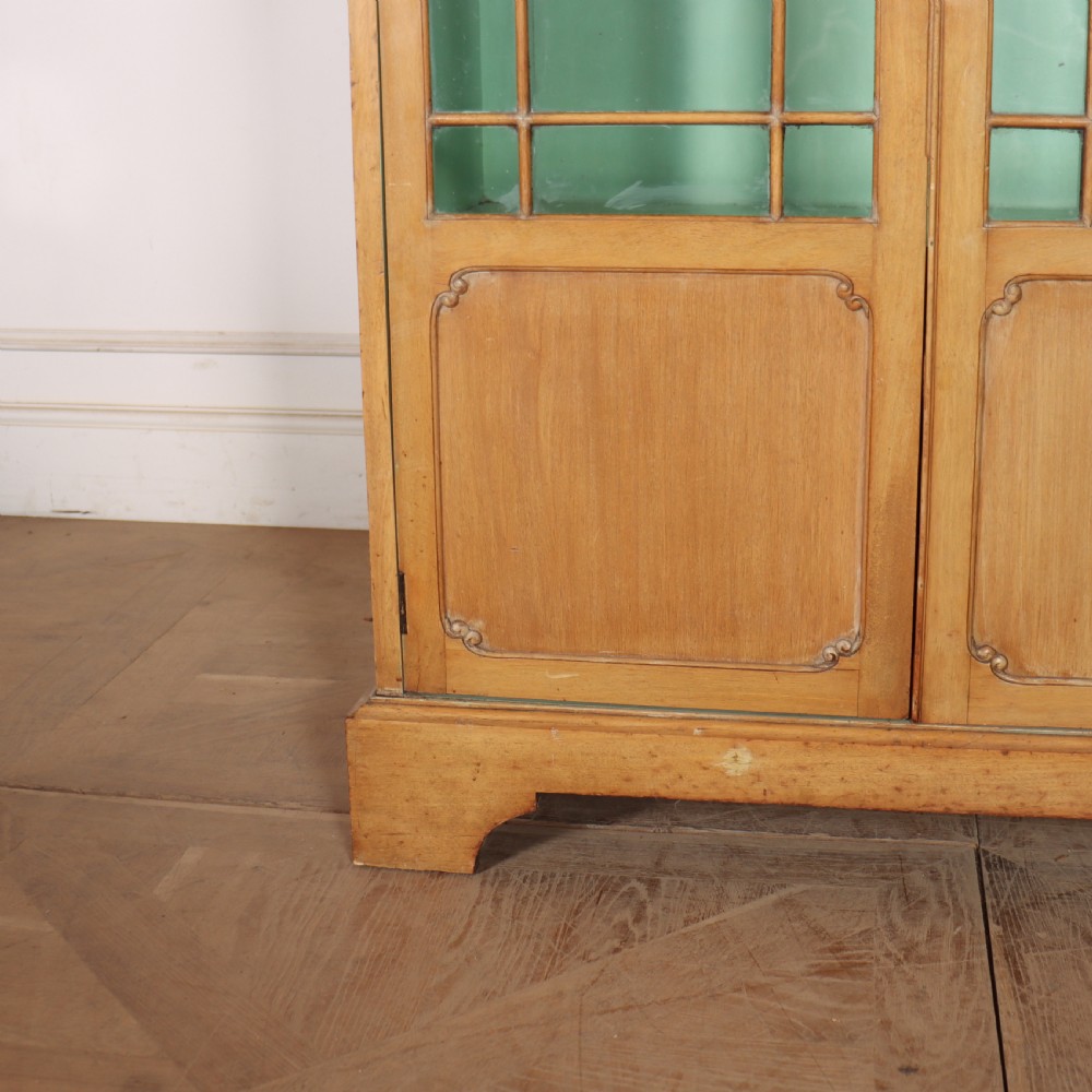 A tall English bleached walnut bookcase featuring two glazed doors with geometric glazing bars, a carved leaf frieze at the top, and a contrasting mint green painted interior. View VI