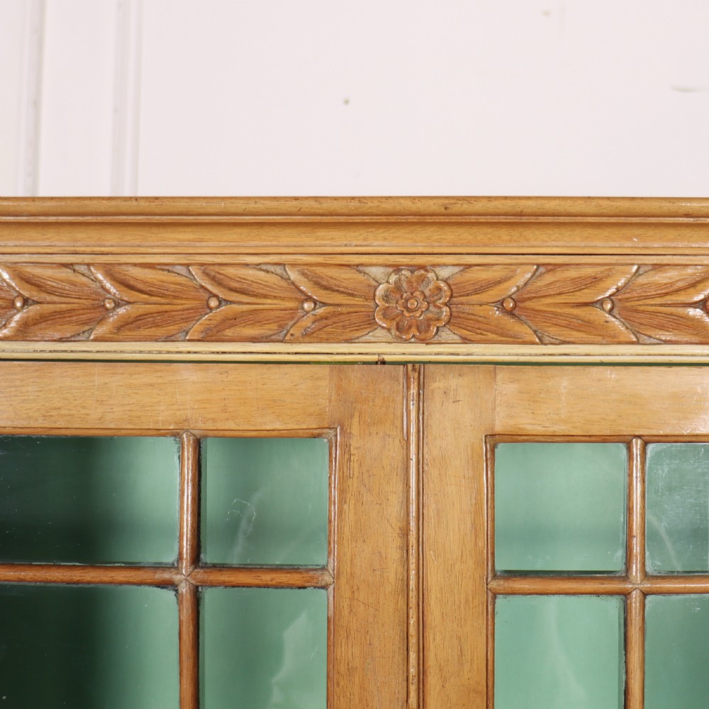 A tall English bleached walnut bookcase featuring two glazed doors with geometric glazing bars, a carved leaf frieze at the top, and a contrasting mint green painted interior. View VII