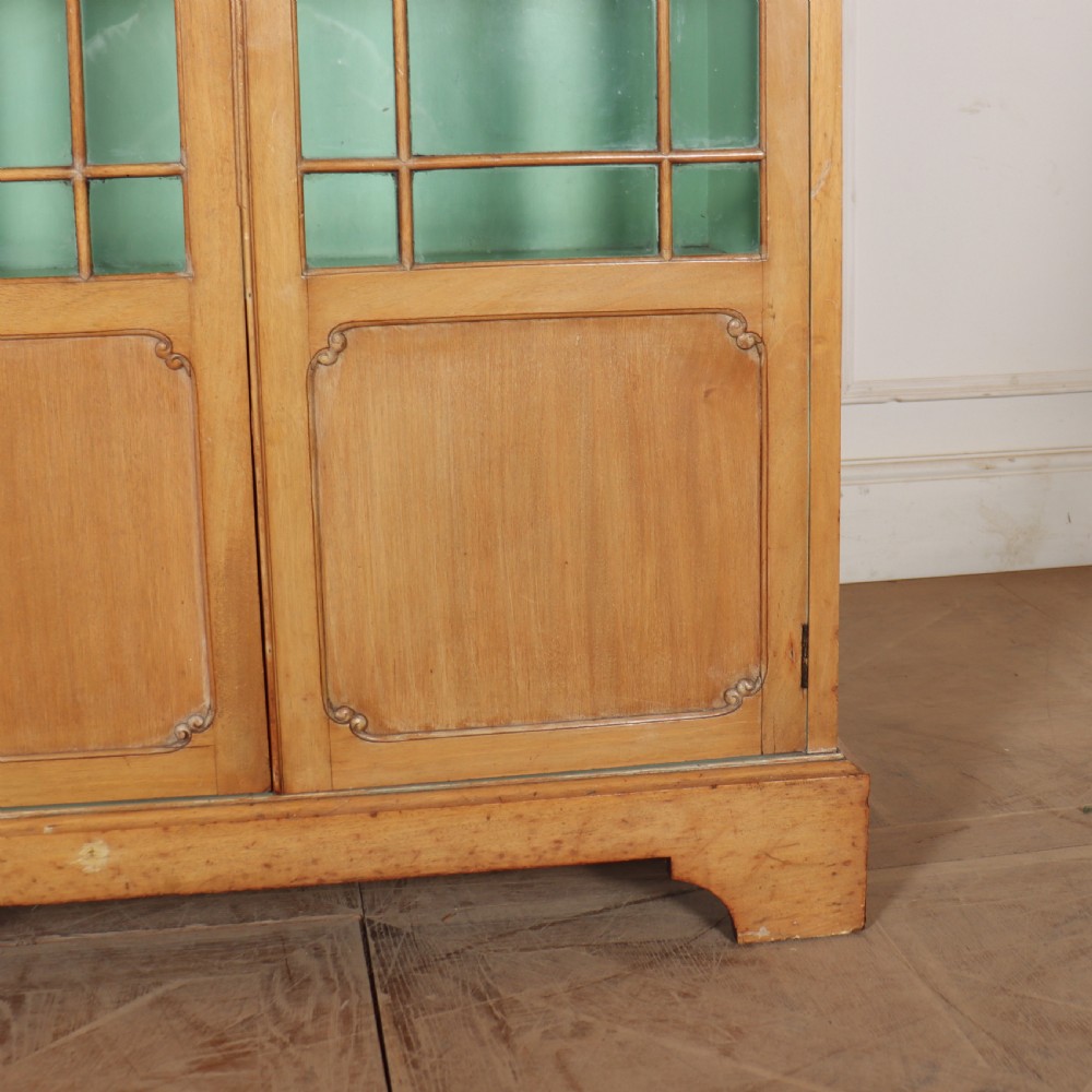A tall English bleached walnut bookcase featuring two glazed doors with geometric glazing bars, a carved leaf frieze at the top, and a contrasting mint green painted interior. View VIII