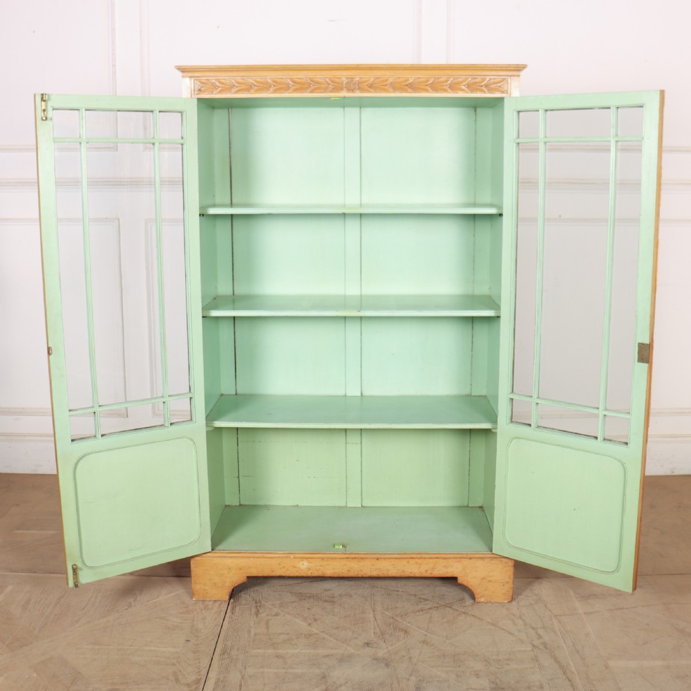 A tall English bleached walnut bookcase featuring two glazed doors with geometric glazing bars, a carved leaf frieze at the top, and a contrasting mint green painted interior. View IX