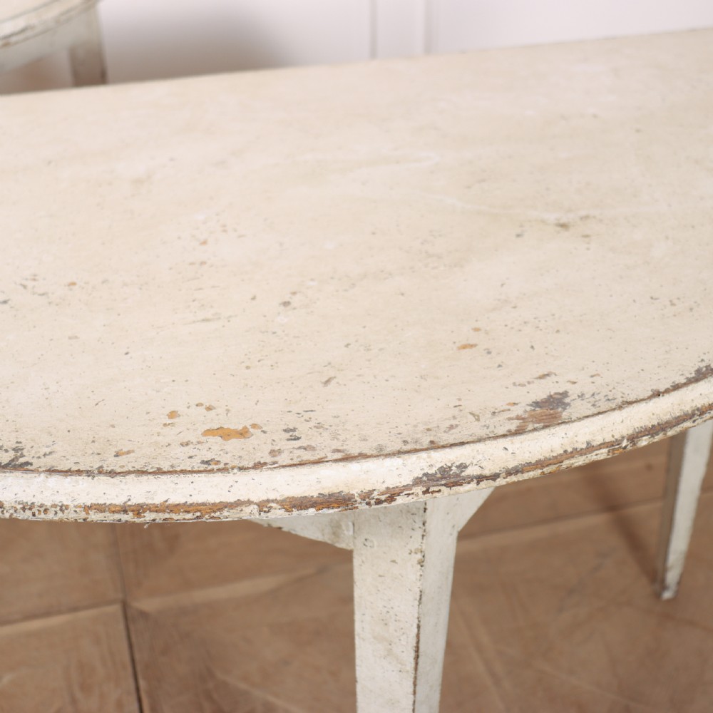 A pair of Swedish demi-lune console tables with distressed off-white painted finish and tapered legs. View V