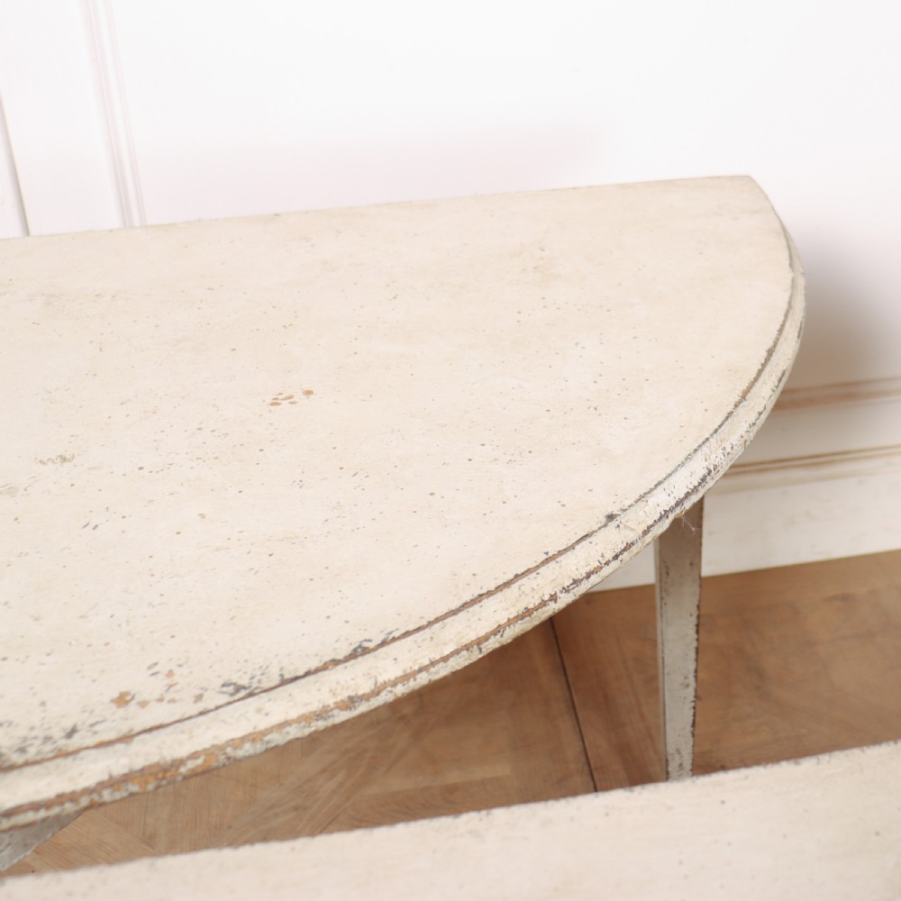 A pair of Swedish demi-lune console tables with distressed off-white painted finish and tapered legs. View VII