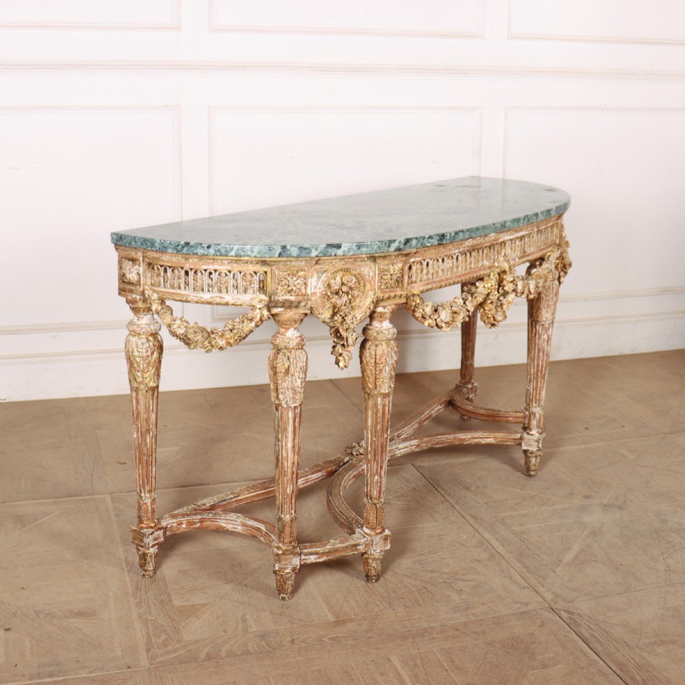 A 19th-century French demi-lune console table featuring a green marble top, ornate carved giltwood frieze with floral swags, and fluted legs.