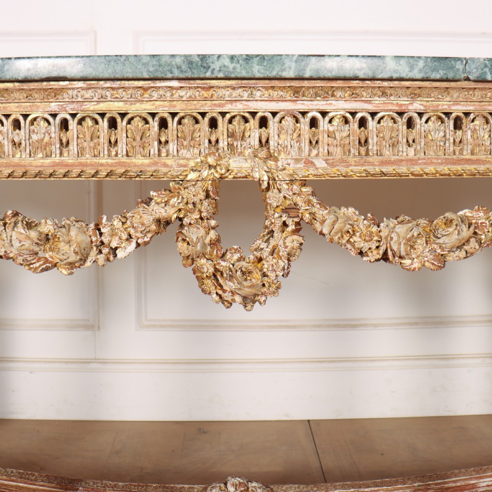 A 19th-century French demi-lune console table featuring a green marble top, ornate carved giltwood frieze with floral swags, and fluted legs. View VI