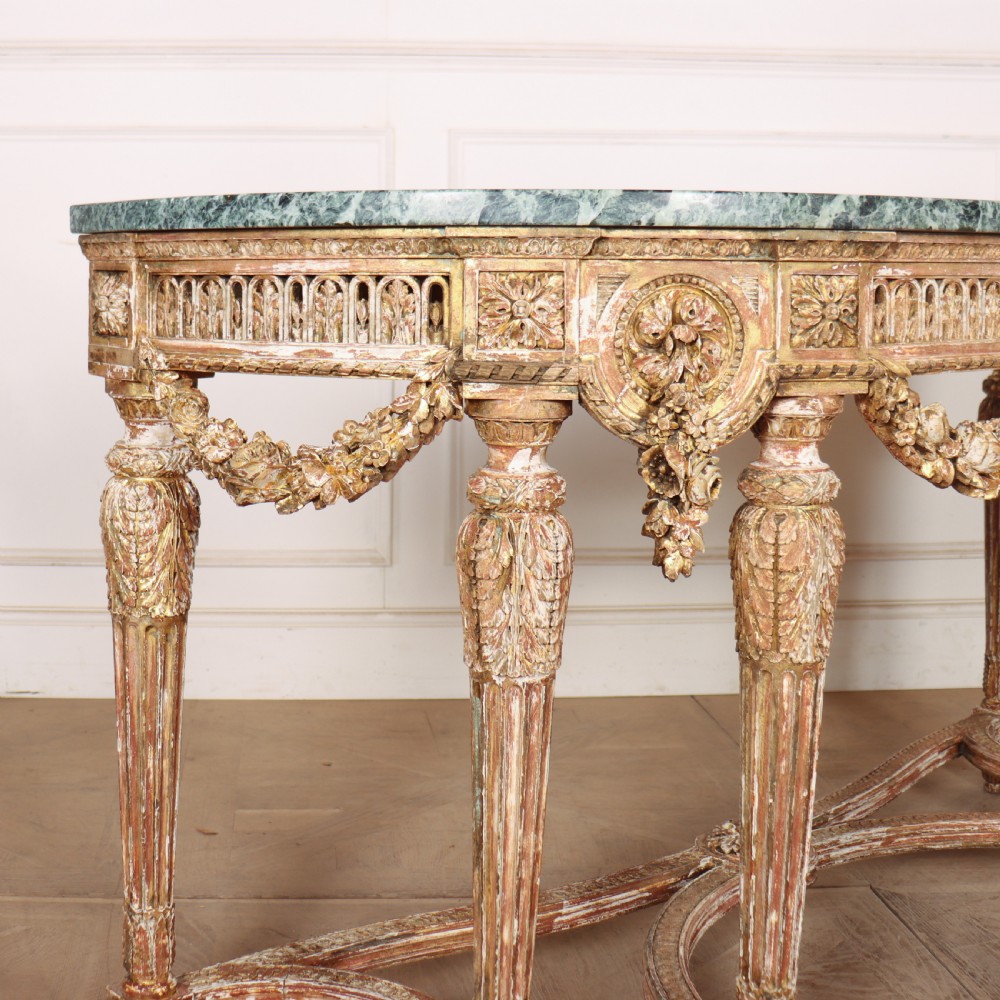 A 19th-century French demi-lune console table featuring a green marble top, ornate carved giltwood frieze with floral swags, and fluted legs. View VII