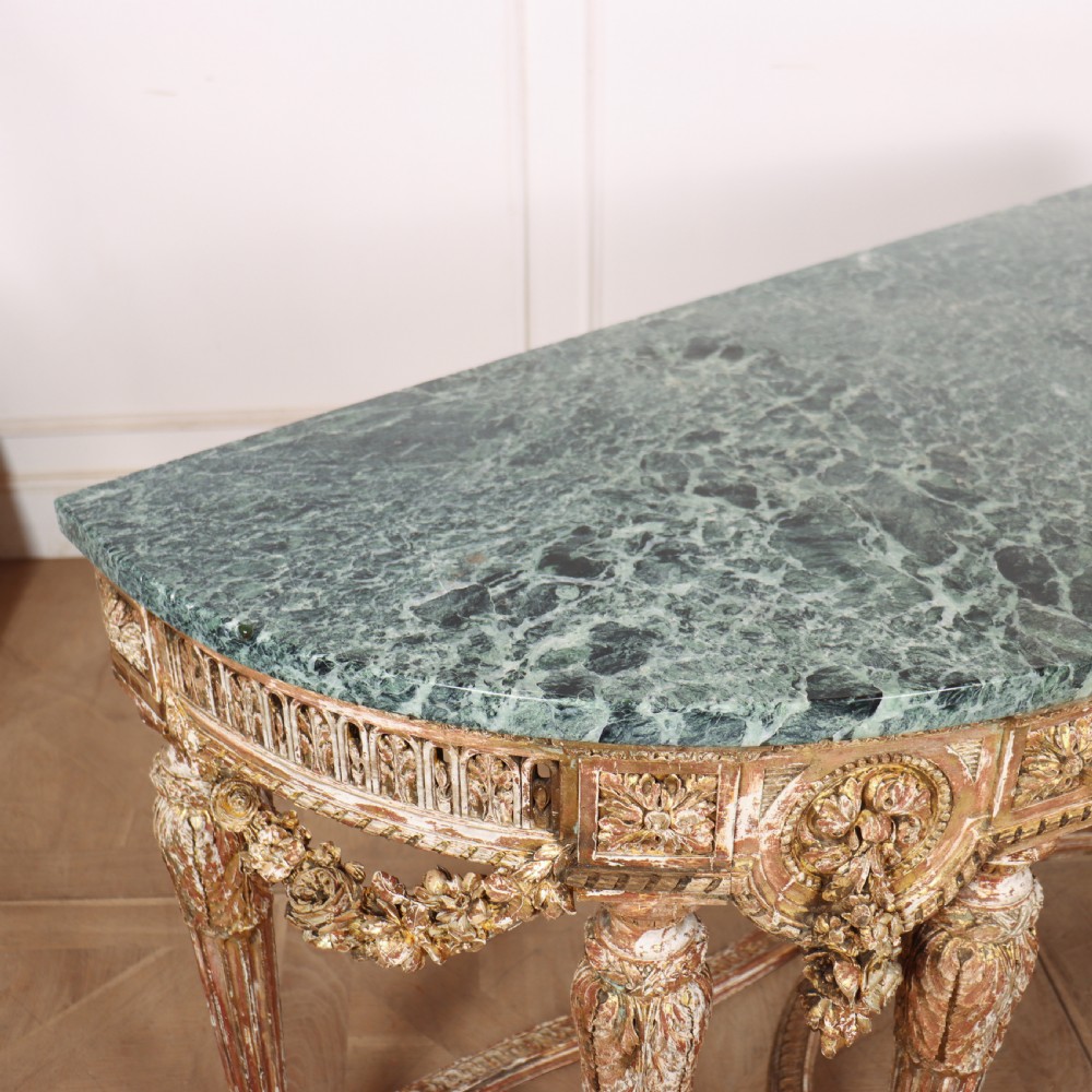 A 19th-century French demi-lune console table featuring a green marble top, ornate carved giltwood frieze with floral swags, and fluted legs. View IX