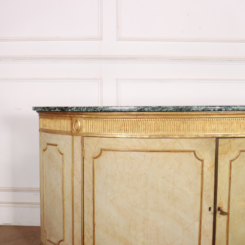 A Neoclassical style cream painted demi-lune side cabinet featuring a dark green marble top, fluted gilded frieze, and panelled cupboard doors. View III