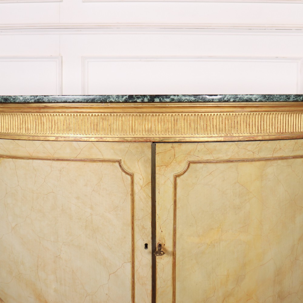 A Neoclassical style cream painted demi-lune side cabinet featuring a dark green marble top, fluted gilded frieze, and panelled cupboard doors. View IV