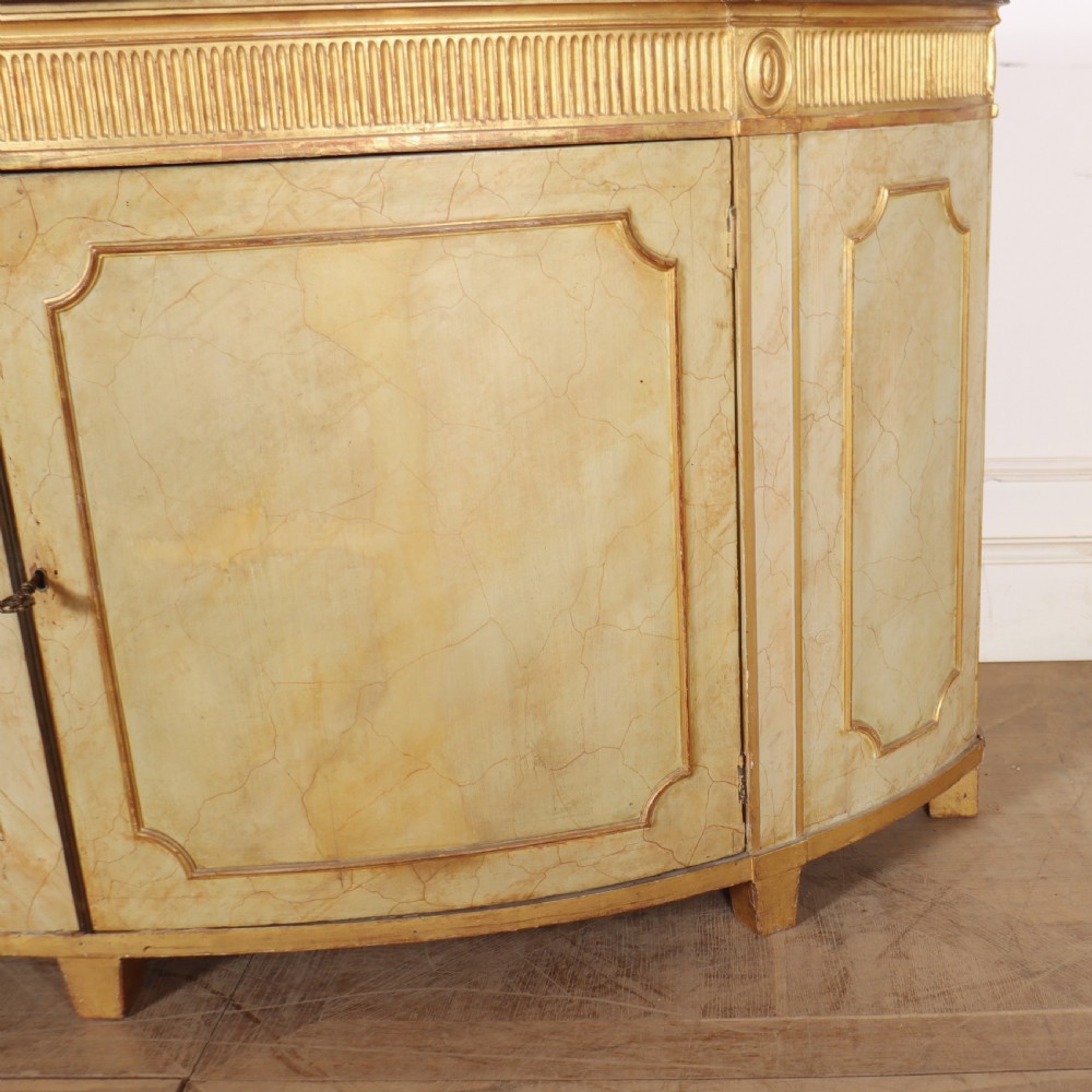 A Neoclassical style cream painted demi-lune side cabinet featuring a dark green marble top, fluted gilded frieze, and panelled cupboard doors. View VI