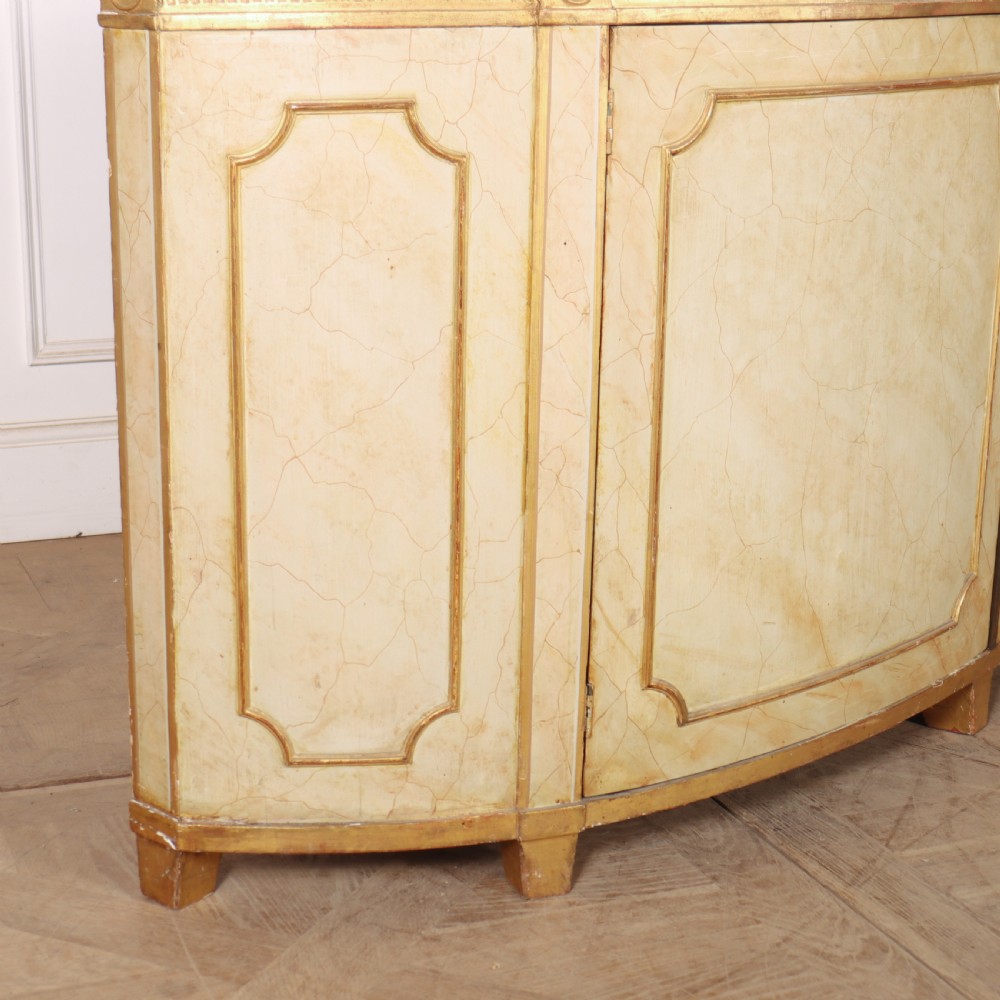 A Neoclassical style cream painted demi-lune side cabinet featuring a dark green marble top, fluted gilded frieze, and panelled cupboard doors. View X